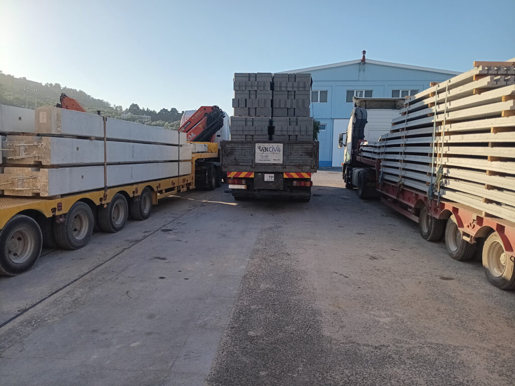 Camiões carregados com elementos pré-fabricados de betão em zona industrial.
